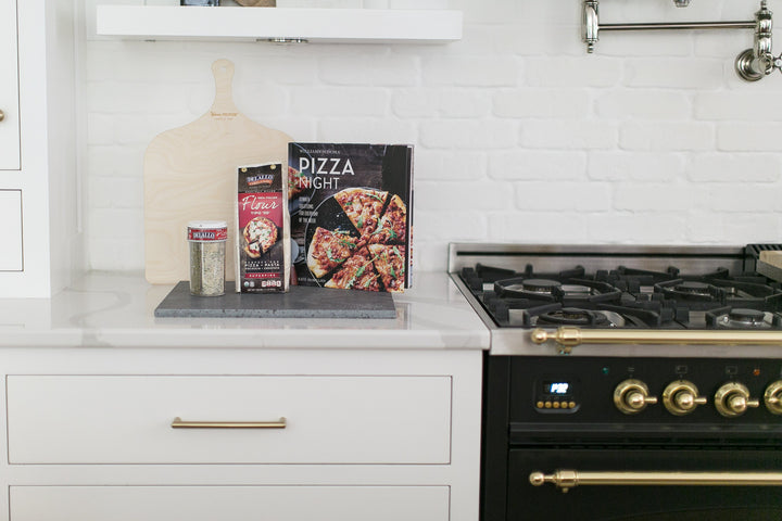 Pizza Peel, Lava Stone, Cookbook, 0.0 Flour, Sauce and Seasoning. The Mario Gift box for Mercy Forest Co. in a white kitchen with Hallman stove.