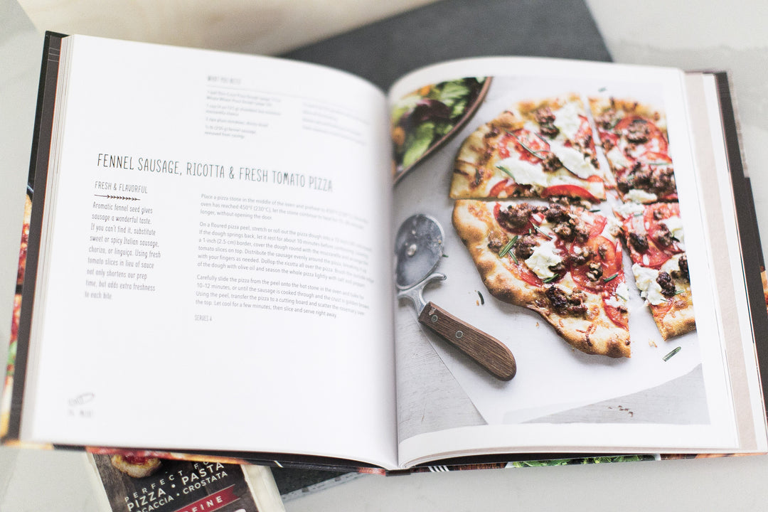 Williams Sonoma Hardcover Pizza Recipe Book open to a Fennel Sausage, Ricotta & Fresh Tomato Pizza recipe. Send this experience style gift today with Mercy Forest Co.