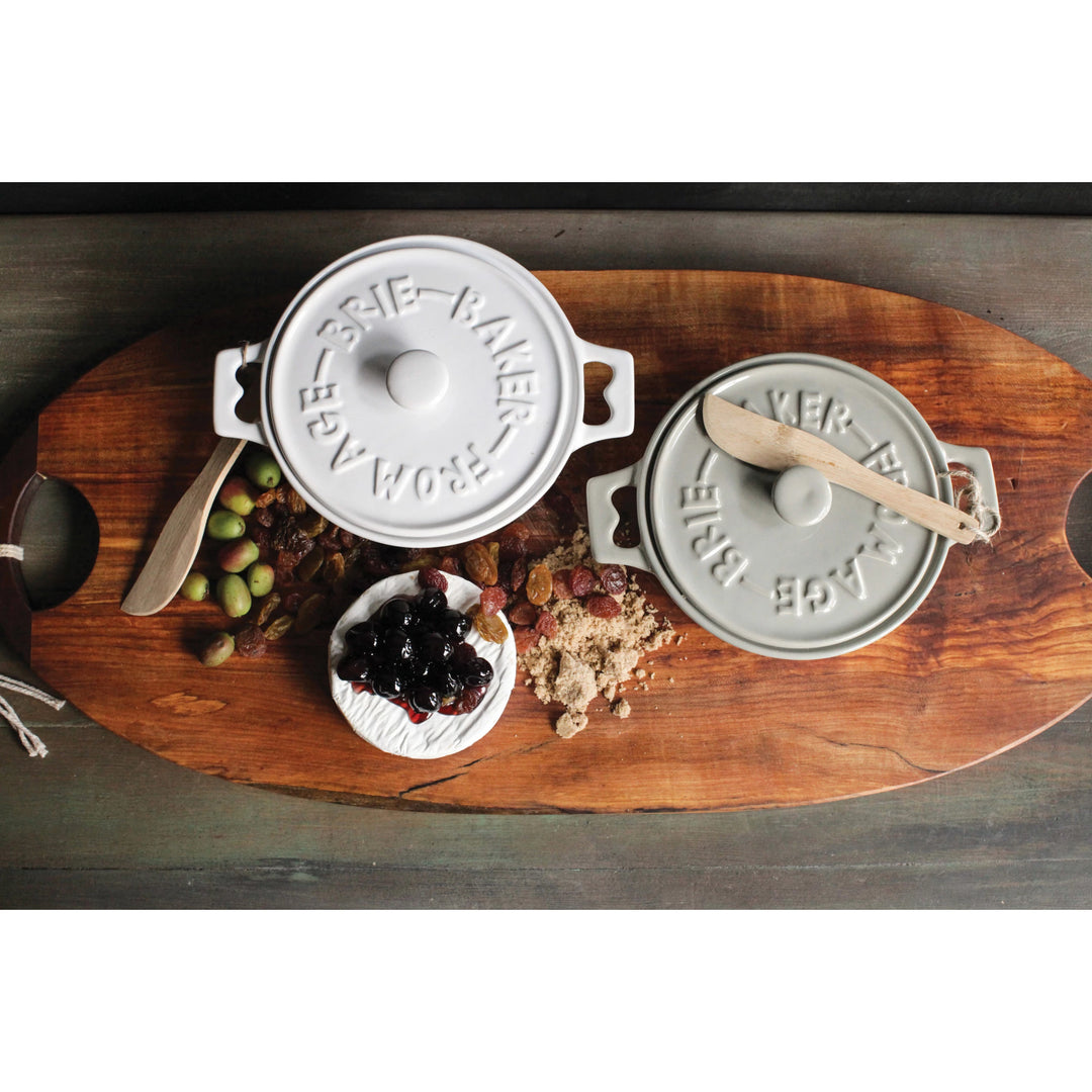 White and grey Brie Bakers with wooden knives on oblong distressed wooden cutting board. Brie cheese, olives, and raisins. Realtor gifts. Housewarming gifts. Client gifts. Mercy Forest Co.