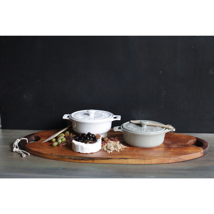 Grey and white brie bakers with wooden knives on top of an oblong wooden cutting board with a wheel of brie, olives, raisins and nuts. Realtor gifts. Housewarming gifts. Mercy Forest Co.