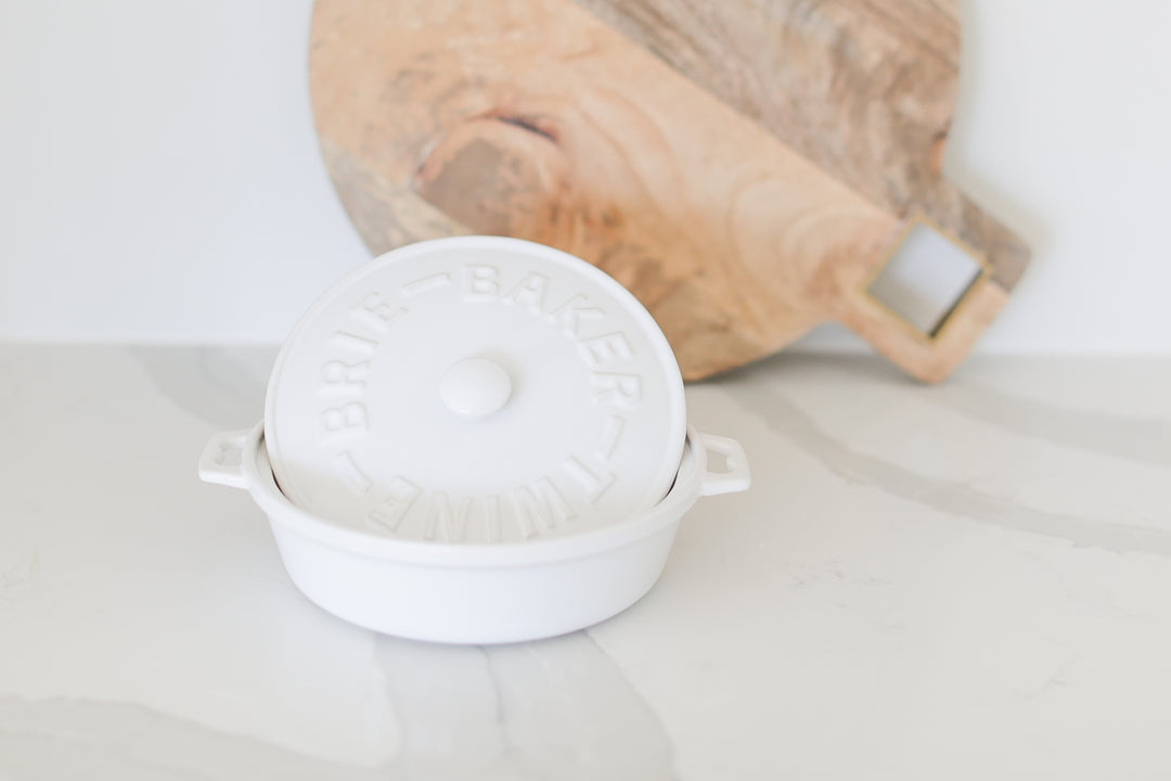 White Brie baker on white and grey marble background with round wooden cutting board in the background. Realtor gifts. Housewarming gifts. Client gifts. Mercy Forest Co.