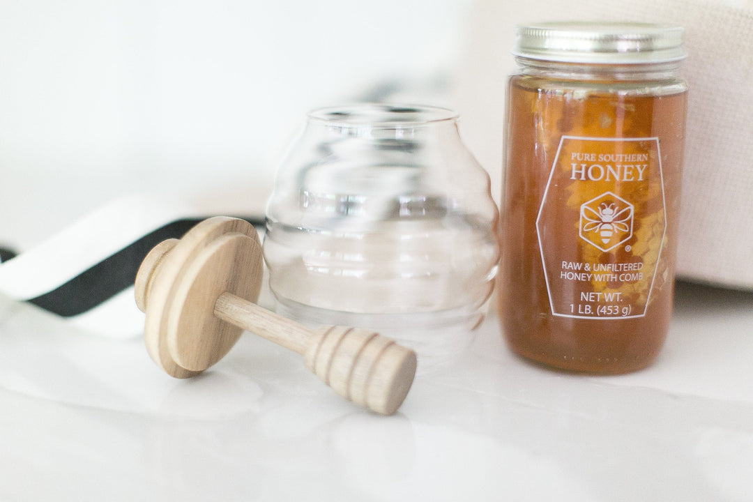 Glass honey jar with a wooden honey dipper and black-and-white ribbon, a simple host gift