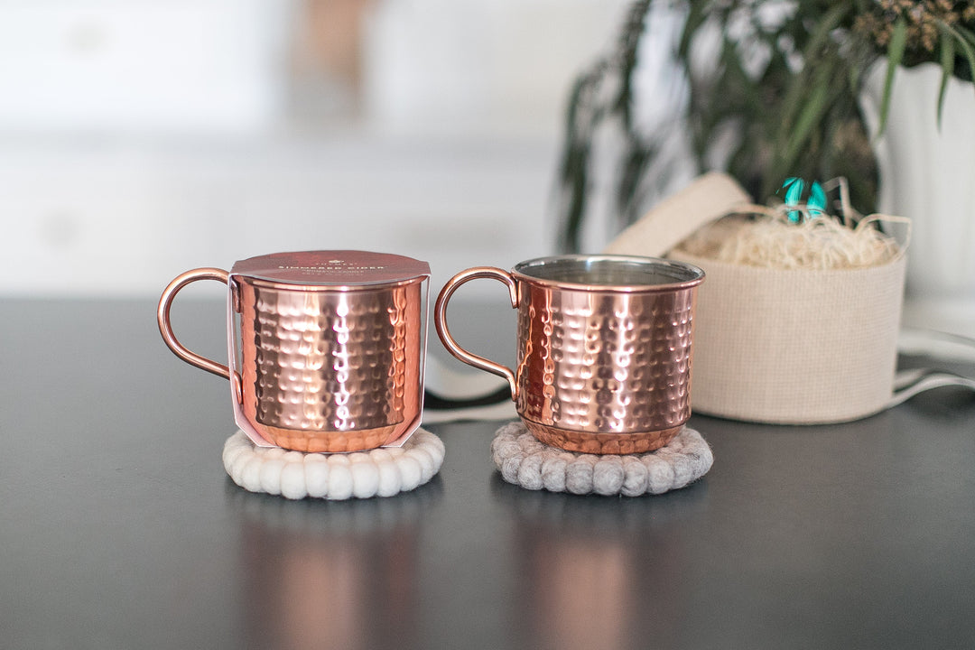 Two copper mugs on white coasters with a blurred background