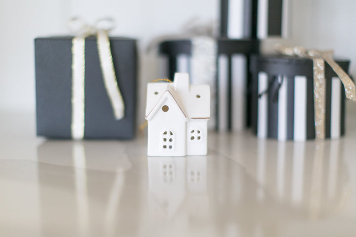 Small white house ornament with black gift boxes on a reflective surface