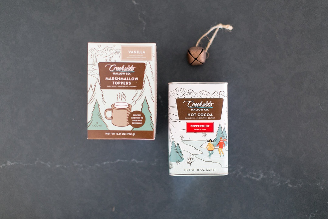 Two boxes of Creekside Mallow Co. hot cocoa and marshmallow toppers on a dark surface.