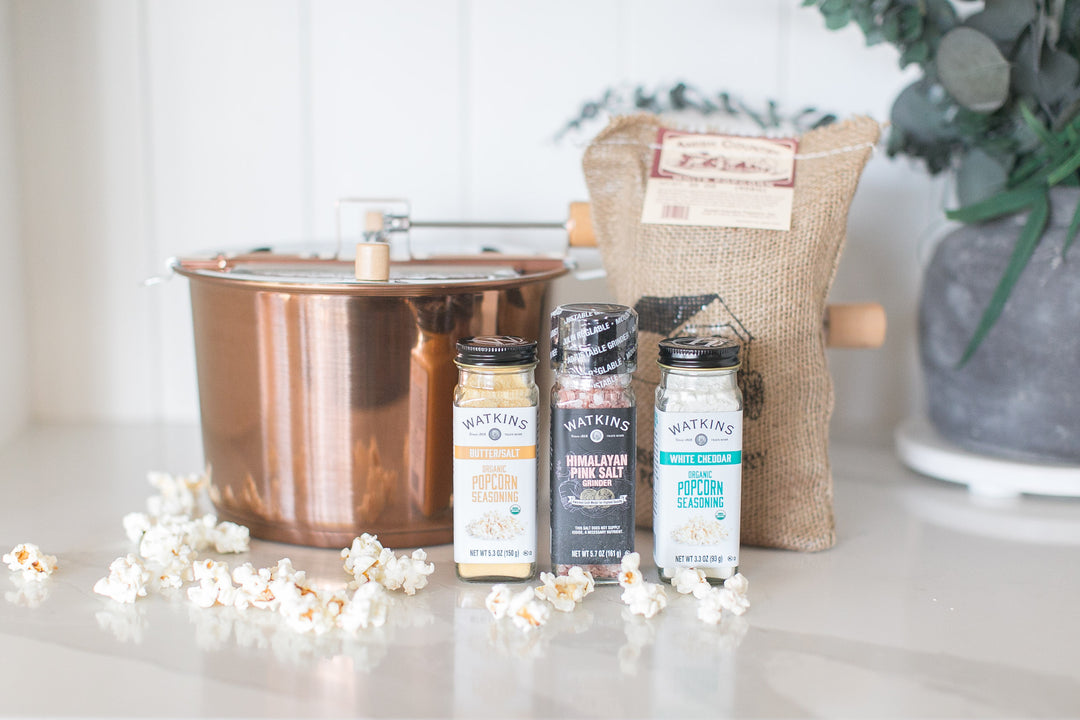 Popcorn-making set with copper pot, popcorn, and seasoning packets on a marble surface.