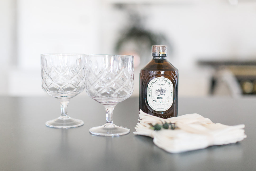 Bottle of Brown French Brut Mojito Mix with two glasses on a table.