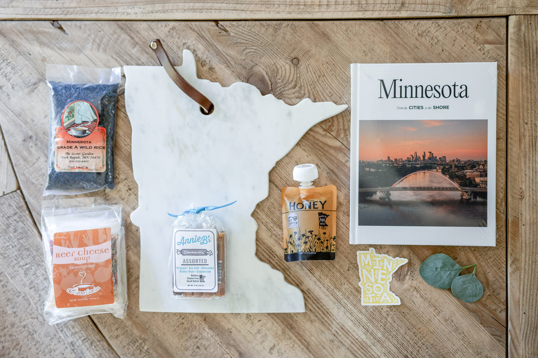 Complete Mercy Forest Co. gift box showcasing all items: Marble Minnesota Board, Annie B's Caramels, Secret Garden Wild Rice, Soup option, Big Dipper Bees Honey Pouch, and a Minnesota coffee table book. Perfect for realtors to present as closing or relocation gifts.
