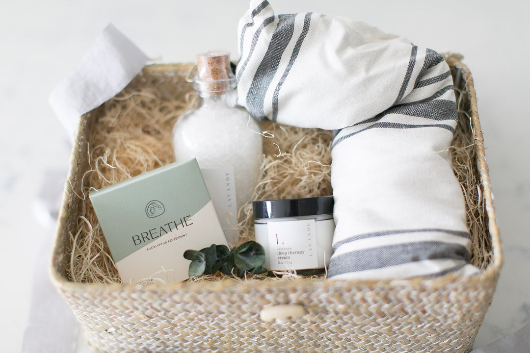 A gift basket containing a lavender eye pillow, a lavender neck pillow, a bottle of lavender salt soak, and a jar of lavender body cream.