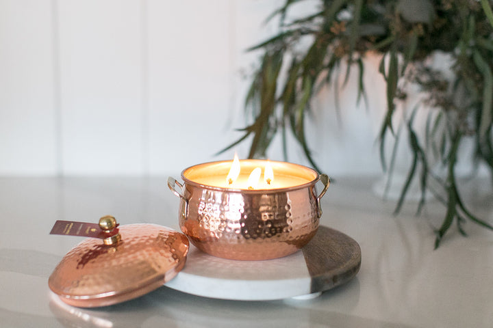 Copper candle holder with a lit candle on a marble trivet, plant in the background