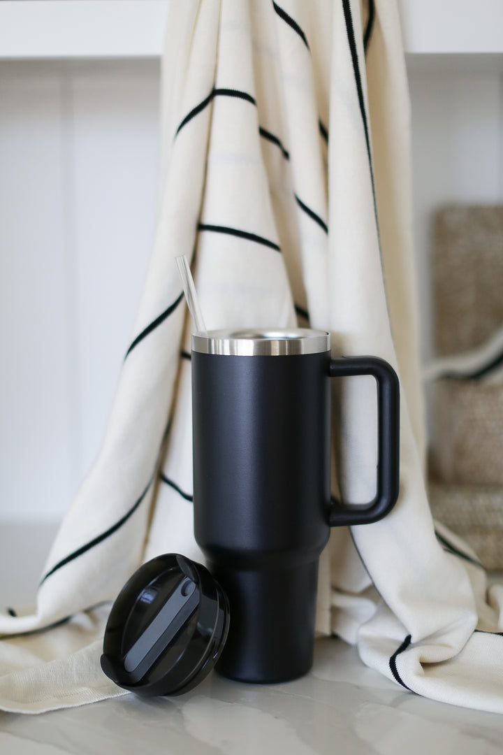 A black 40oz tumbler with a handle, cover, and straw. On a marble countertop and a striped towel behind.