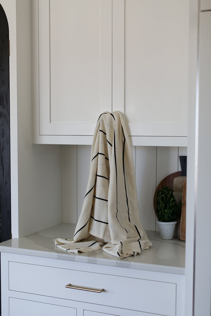 A cream and black striped blanket hung on a white cabinet.