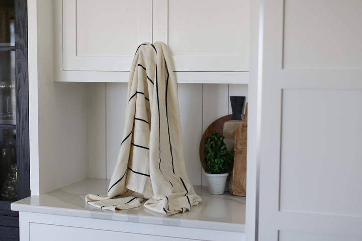 A striped cream/black blanket  draped from a white cabinet. Other cutting boards and cabinets in the background.