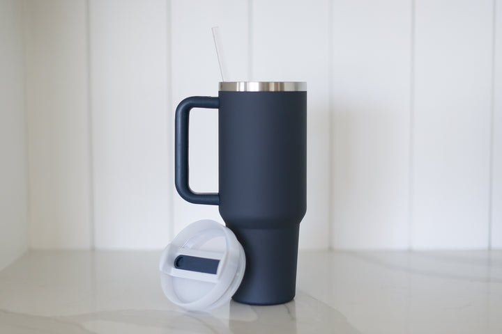 A navy 40oz tumbler with straw and handle. A shiplap and marble background.