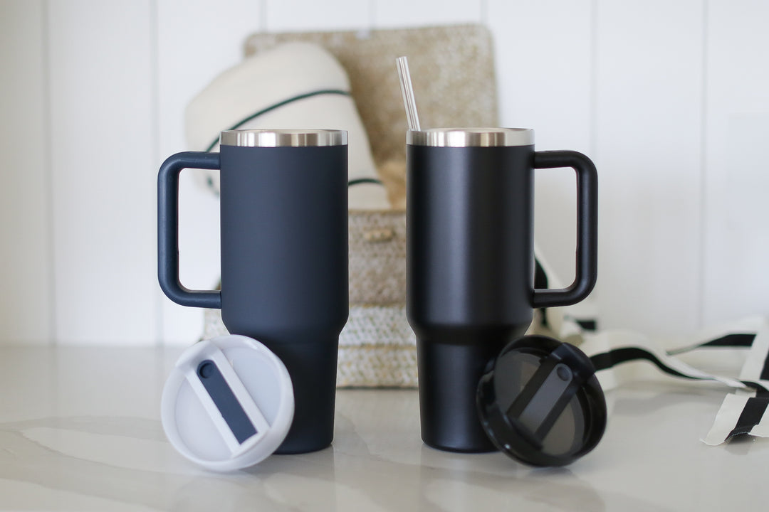 A navy and a black 40oz Tumbler with Handles with their covers off. Sitting on a marble counter with shiplap background and a giftbox behind.