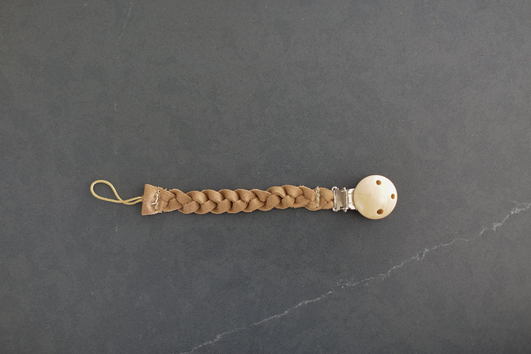 A leather binky holder that has a clip on a dark countertop.