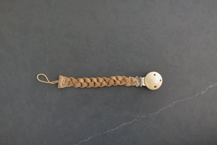 A leather binky holder that has a clip on a dark countertop.