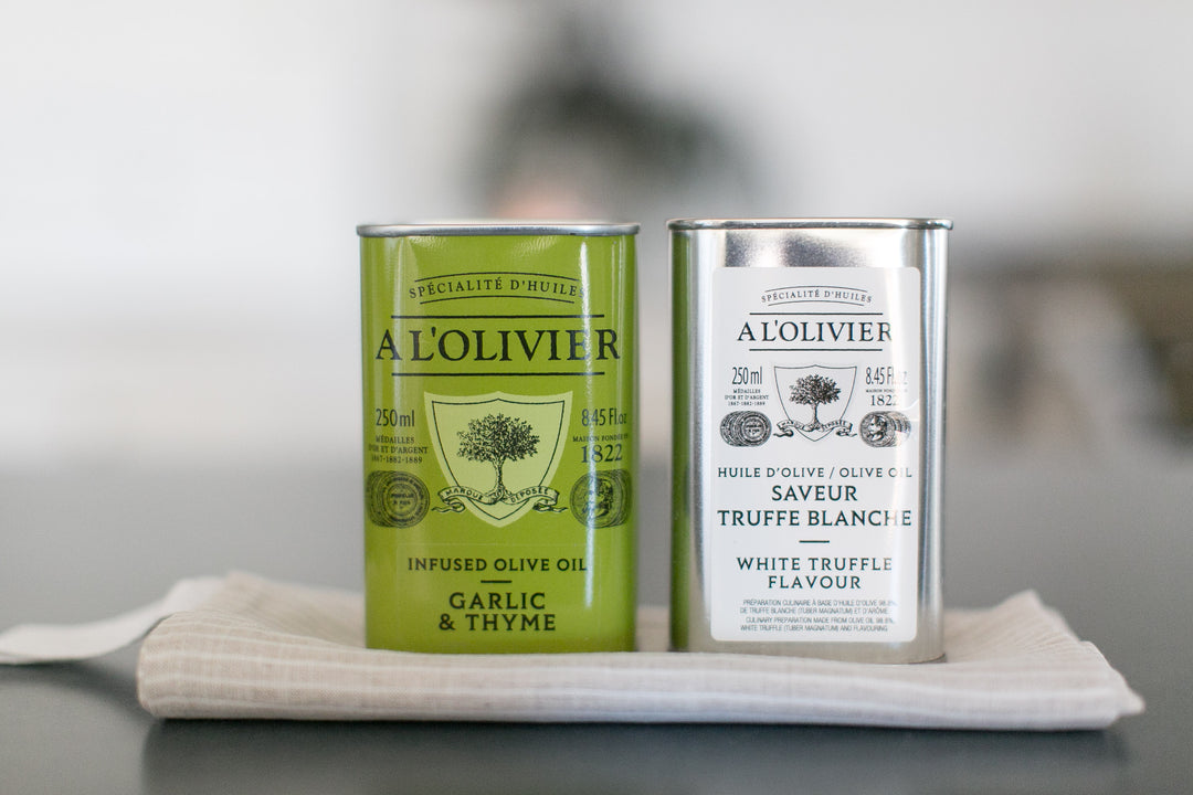 Two tins of A'L Olivier olive oil on a white cloth with a blurred background