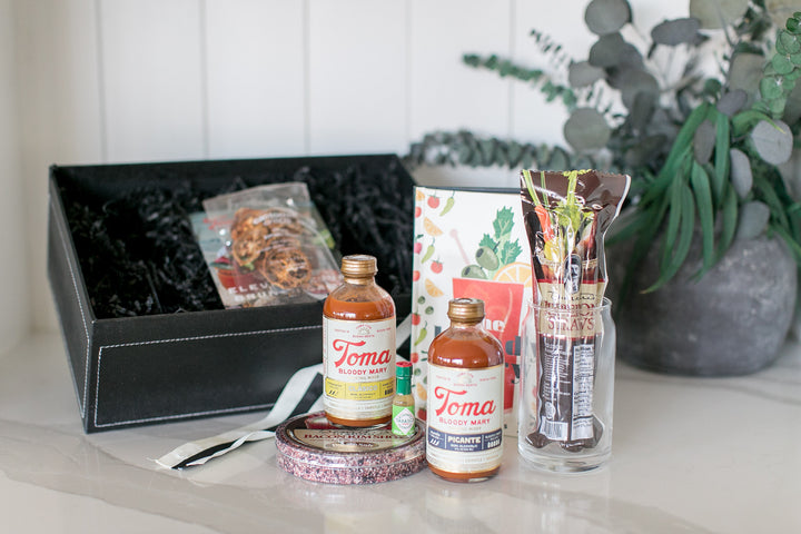 Toma bloody Mary mix bottles with packaging on a table with drink accompaniments 