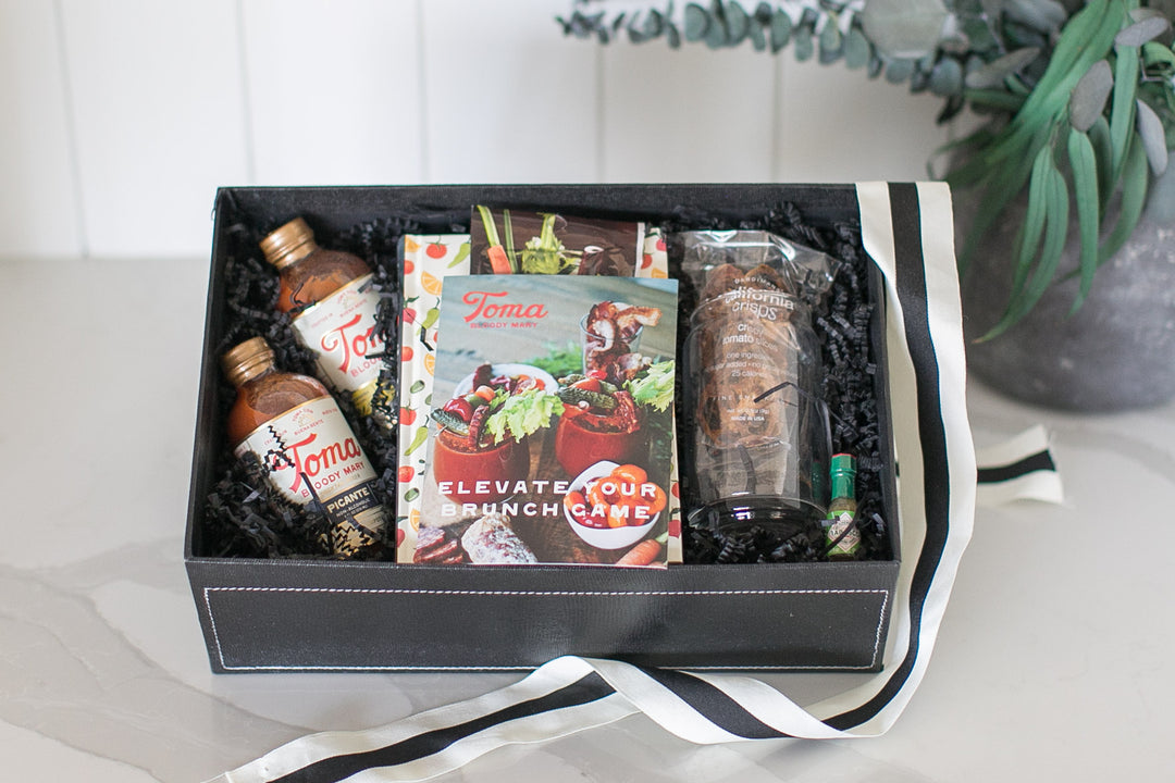 Bloody Mary Themed Gift box with Toma Bloody Mary Mix, and products on a white surface with a plant in the background