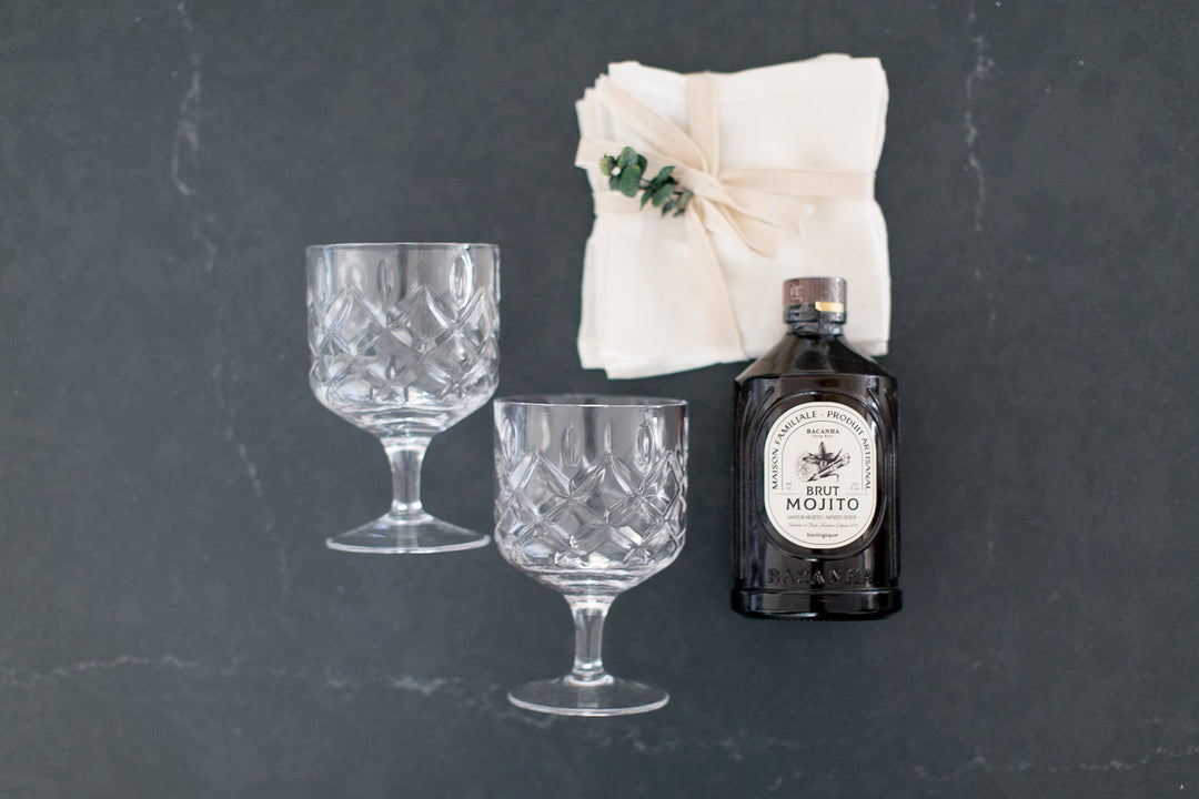 Two glass goblets and a bottle of French Mojito Mix on a dark surface with a white cloth napkins.
