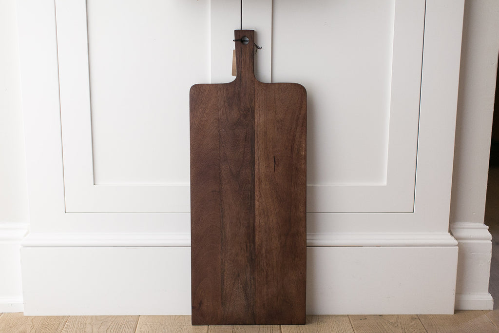 Wooden cutting board hanging on a white paneled wall.