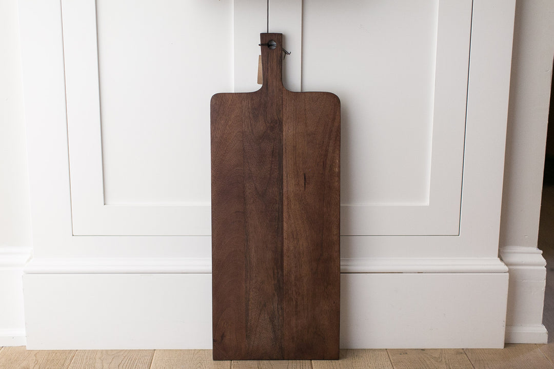 Wooden cutting board hanging on a white paneled wall.