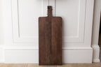 Wooden cutting board hanging on a white paneled wall.
