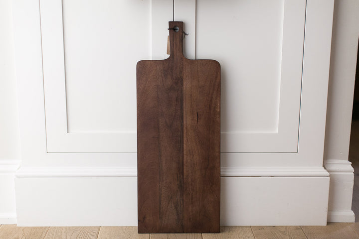 Wooden cutting board hanging on a white paneled wall.