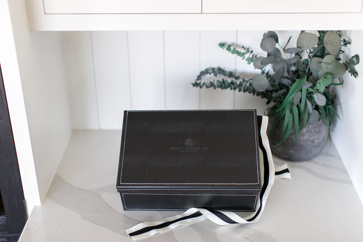 Black leather-bound book with a ribbon marker on a white surface, next to a vase of flowers.