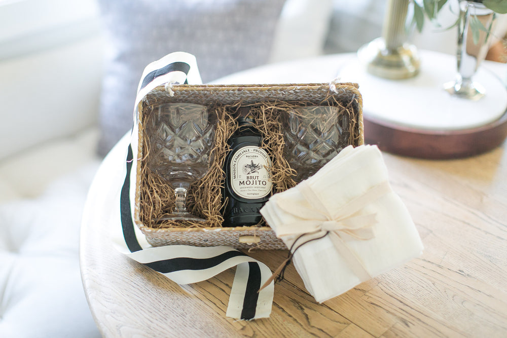 Mojito bottle in a decorative box with glassware and napkins on a wooden table