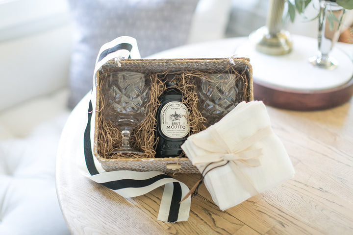 Mojito bottle in a decorative box with glassware and napkins on a wooden table
