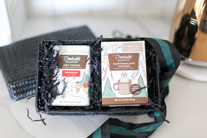 Two packages of Creekside Mallow Co. hot cocoa and marshmallow toppers in a black gift box on a white surface.