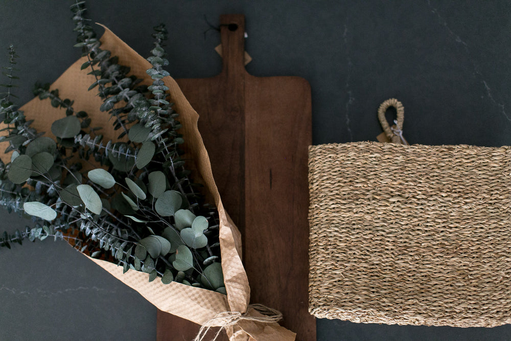 Bouquet of eucalyptus leaves with a wooden cutting board and woven basket on a slate countertop surface