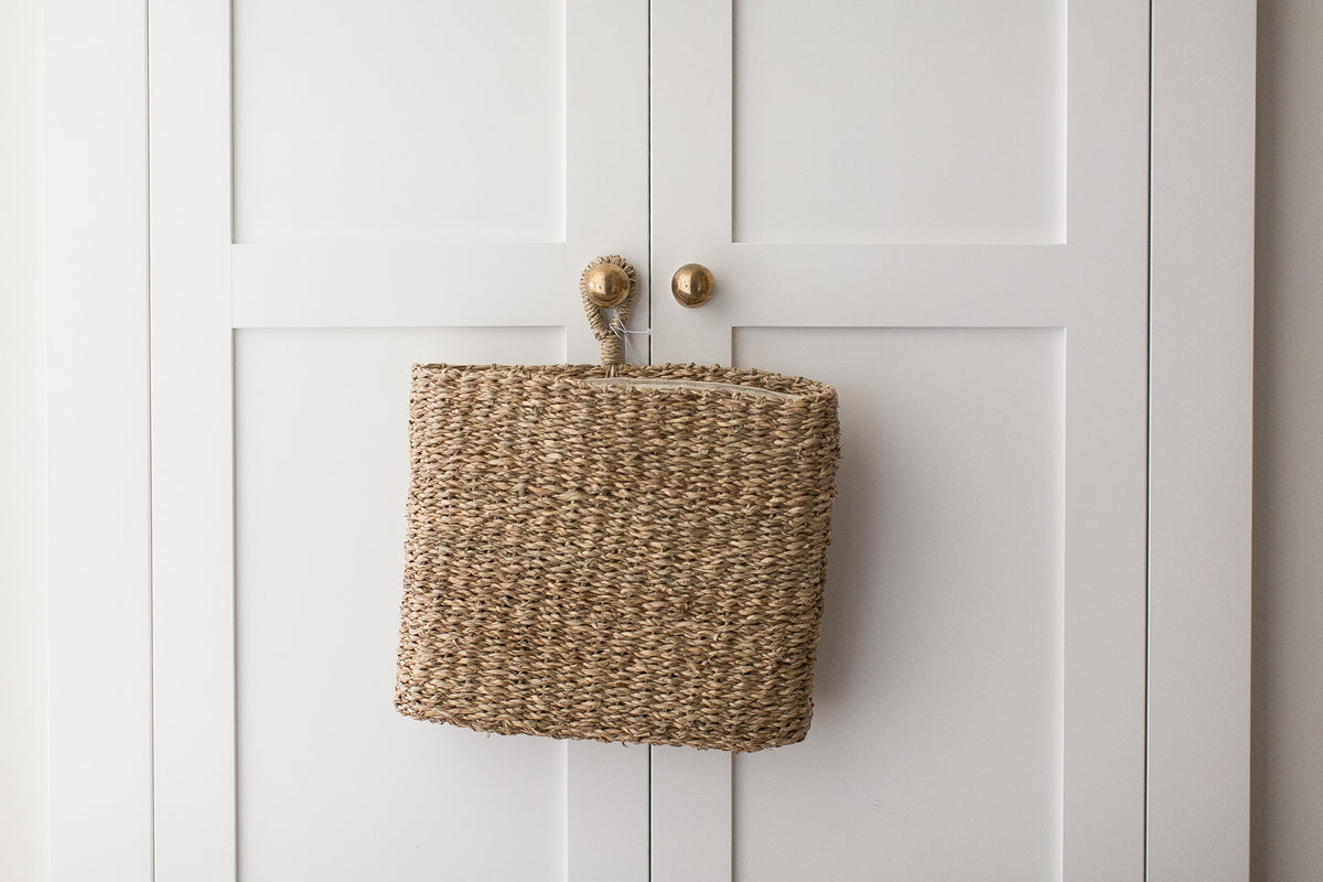 Woven basket attached to a white cabinet with brass knobs.