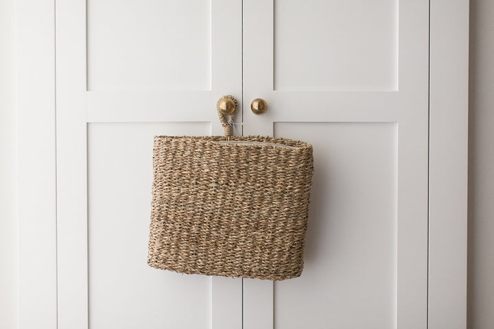 Woven basket attached to a white cabinet with brass knobs.