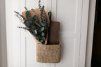Woven basket with preserved eucalyptus greenery and a wooden cutting board on a white paneled cabinet.