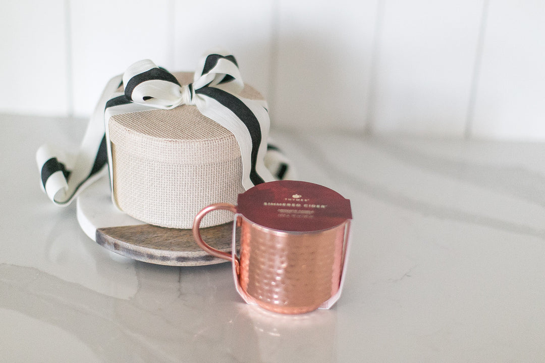 Rose gold mug with a brand label on a white surface next to a decorative box.