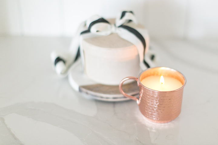 Copper mug with a lit candle on a marble surface with a blurred background