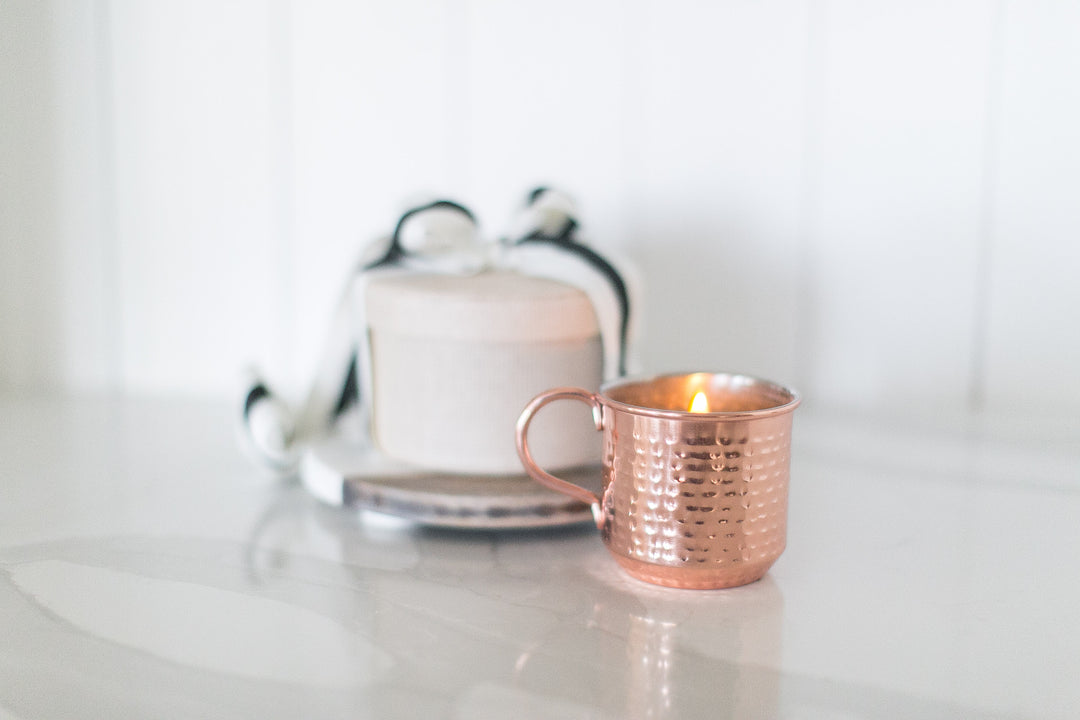 Rose gold mug with a lit candle on a white surface