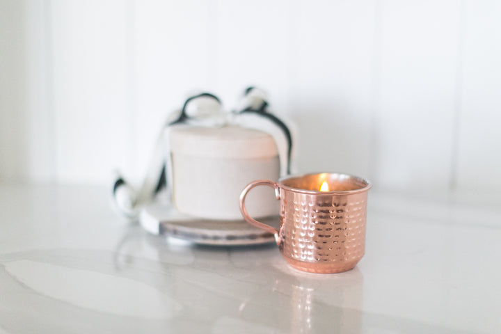 Rose gold mug with a lit candle on a white surface