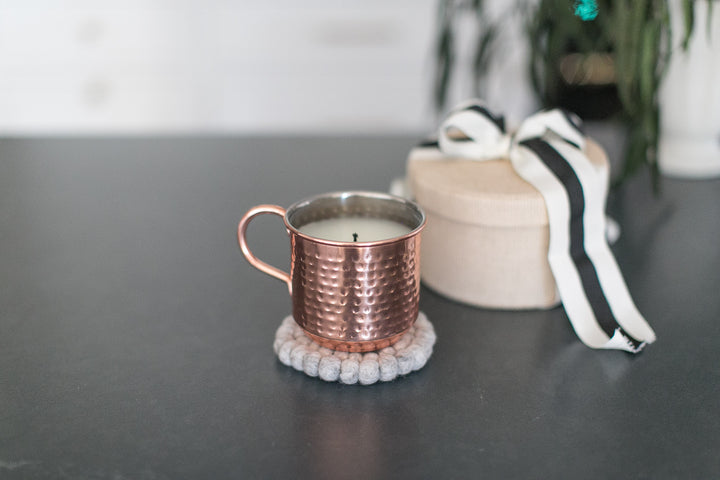 Copper mug with a candle on a textured coaster on a dark surface.