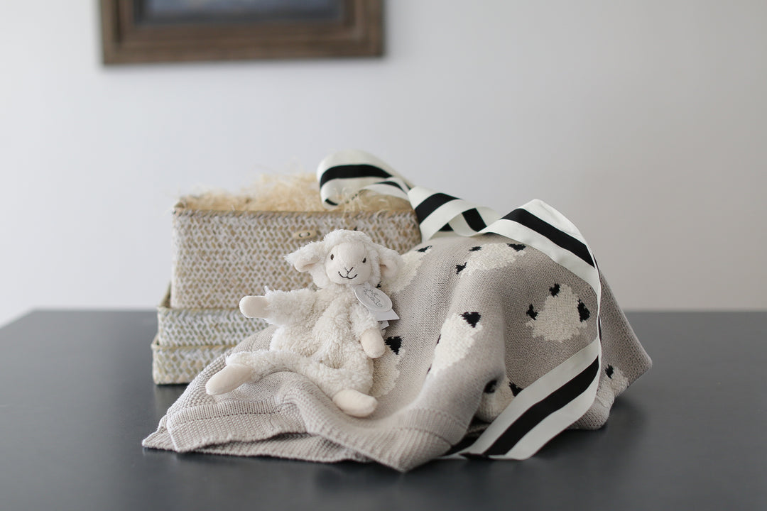 Lamb baby blanket with lamb plush lovie. wrapped in a whitewashed woven basket with lid. set on a black countertop. 