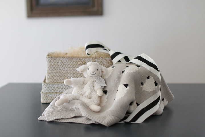 Lamb baby blanket with lamb plush lovie. wrapped in a whitewashed woven basket with lid. set on a black countertop. 