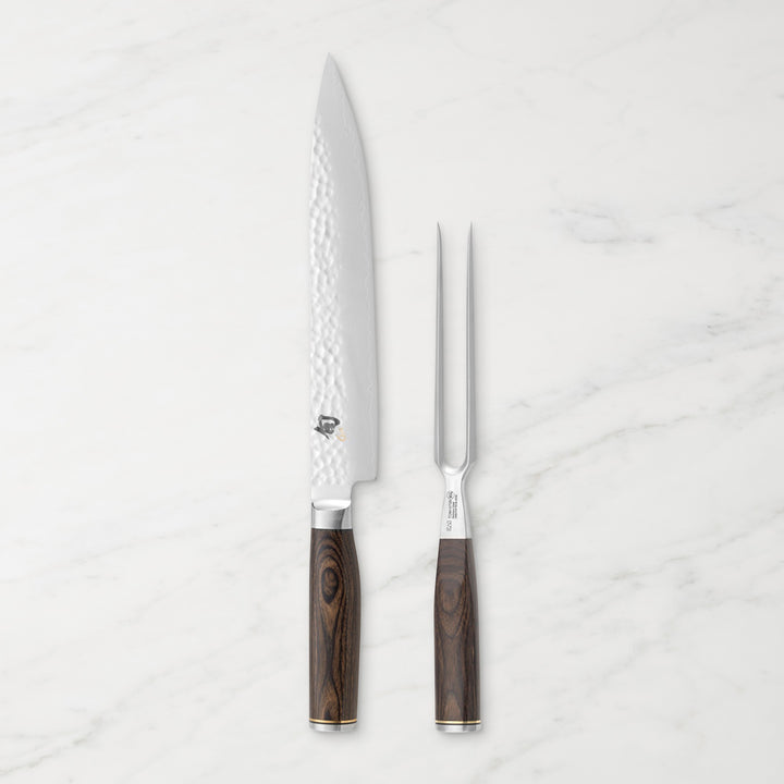 Shun Premier Carving knife and fork with walnut handle set side by side on a white marble backdrop