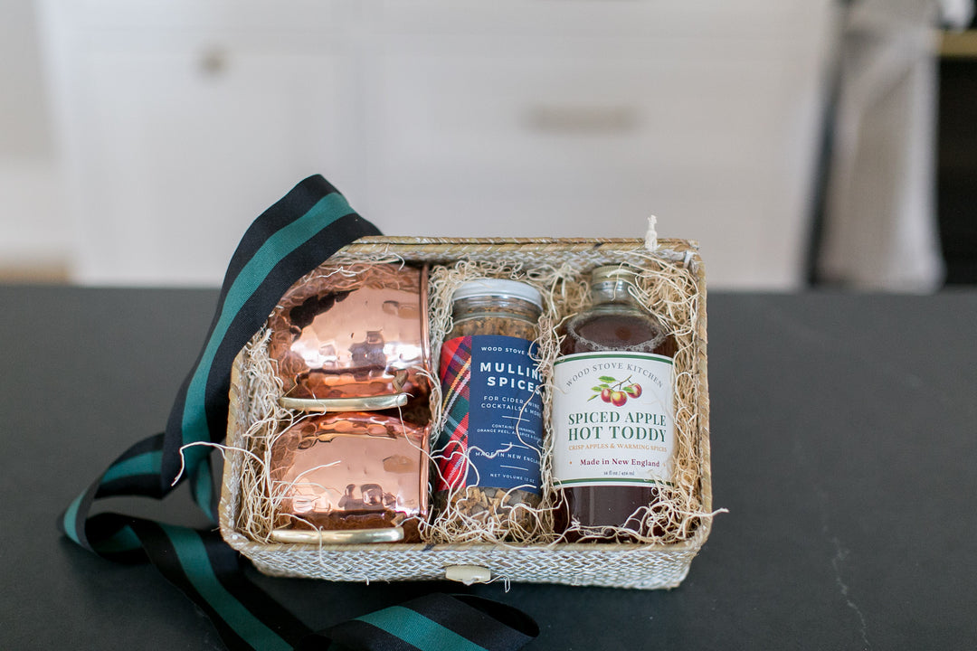 Gift basket with copper mug, jar of mulling spices and apple cider hot toddy on a dark slate surface.