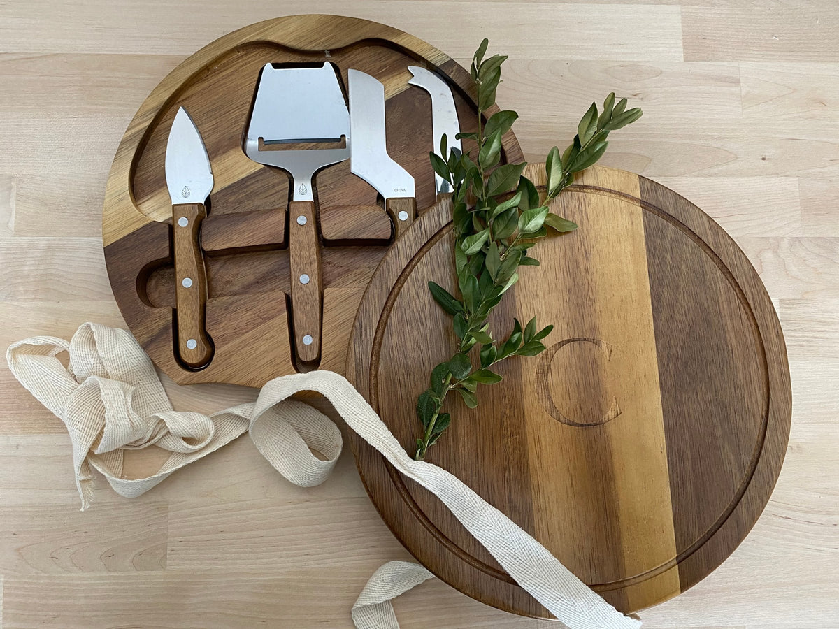 Acacia cheese board with a laser-engraved "C" and a four-piece knife set, with boxwood and cream ribbon.