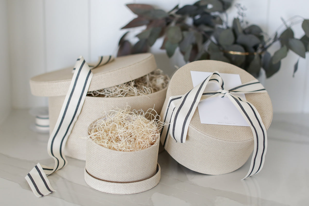 Three linen hat boxes with black-and-white striped ribbon and a Mercy Forest Co. gift card, beside eucalyptus