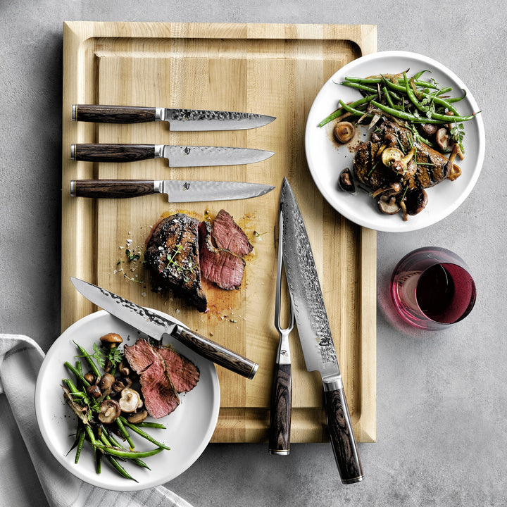 Set of Shun Premier Carving knives with shun premier steak knives on a cutting board with steak and green beans