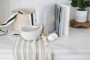 Curated gift box with stoneware bowl, whisk with wooden handle, bistro apron and egg recipe book. Gift is ready to ship and sent in beautiful round woven box and with a hand written note. Mercy Forest Co. 